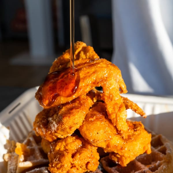 Maple syrup drizzling over a stack of crispy fried chicken and waffles.