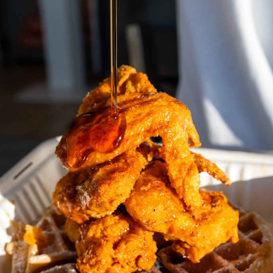 Maple syrup drizzling over a stack of crispy fried chicken and waffles.