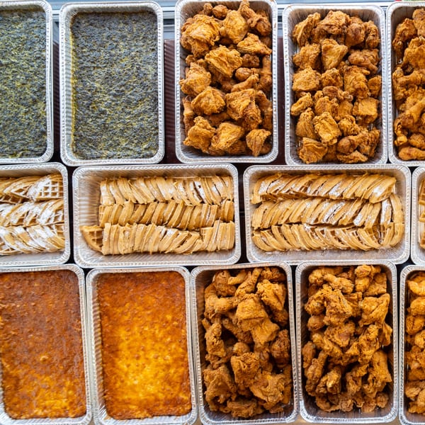Multiple foil trays filled with Southern Style Chicken & Waffle's fried chicken, waffles, and sides.