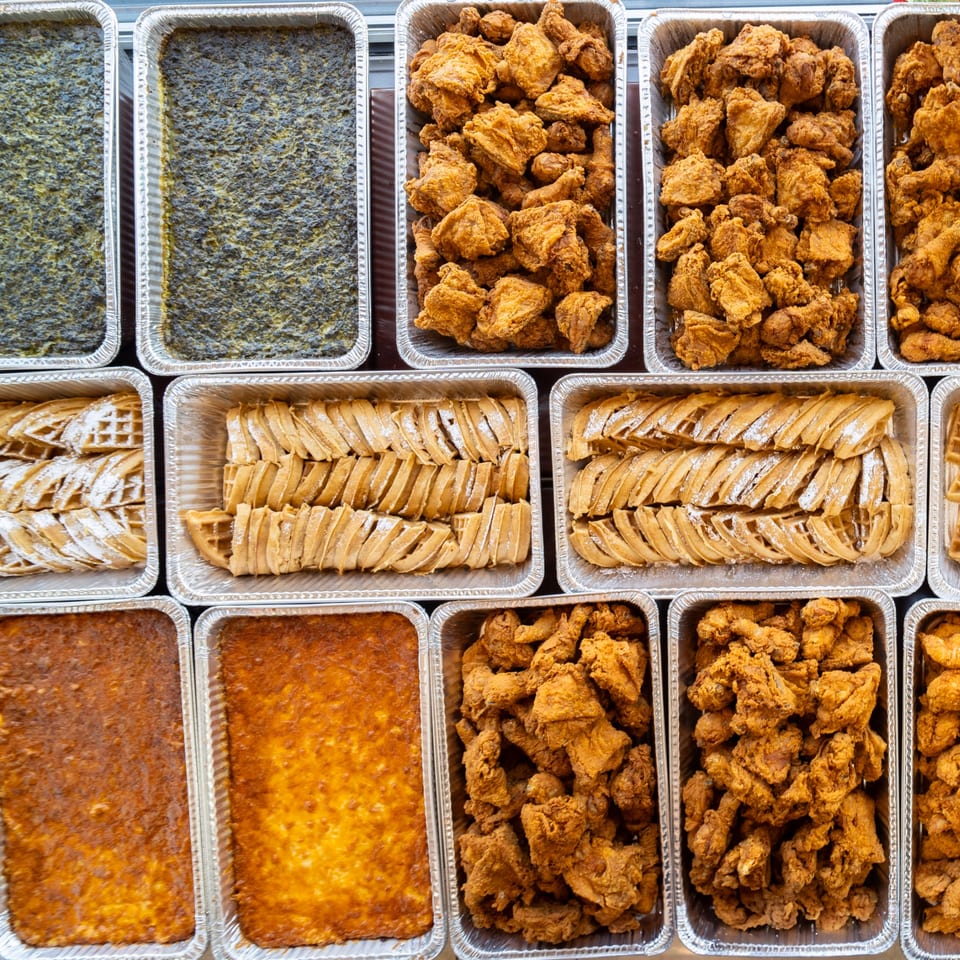 Multiple foil trays filled with Southern Style Chicken & Waffle's fried chicken, waffles, and sides.