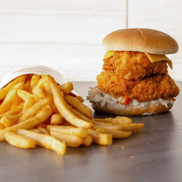 Crispy double chicken sandwich with cheese and coleslaw next to a pile of golden french fries.