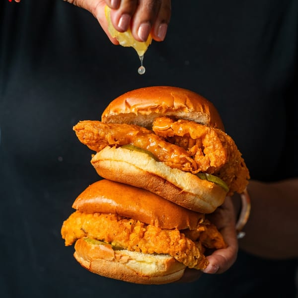 Two stacked Southern Style Chicken & Waffle sandwiches, with a hand squeezing lemon juice over them.