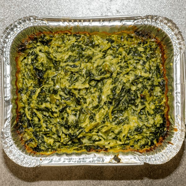 Creamy baked spinach in a rectangular aluminum foil pan, a side dish from Southern Style Chicken & Waffle.