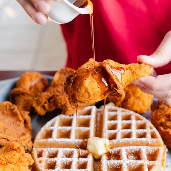 Maple syrup being poured over a piece of fried chicken and a waffle with butter.